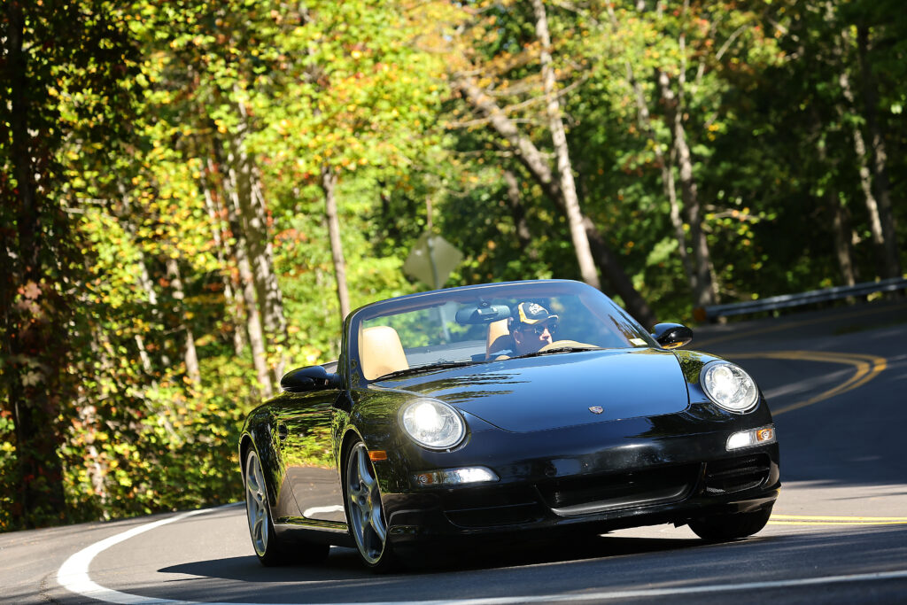 Keith Bloom driving a black Porsche 911 Cabriolet through an autumn curve on the Tail of the Dragon at Deals Gap — fall foliage lining the road through the Great Smoky Mountains